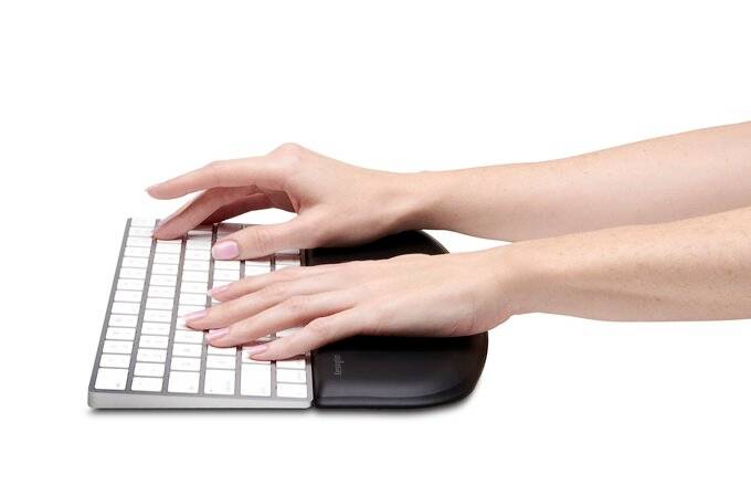 A person is typing on a sleek white keyboard, using a grey wrist rest for support.
