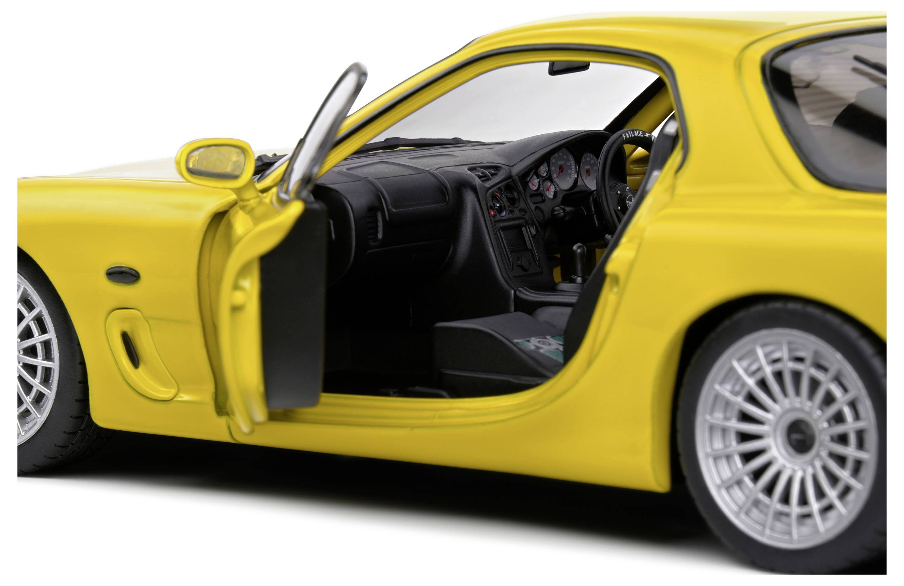 Yellow sports car with open driver's door, interior visible, showing steering wheel and dashboard details.