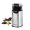 A silver electric coffee grinder with a black lid sits next to coffee beans and ground coffee; brand name 'emerio'.