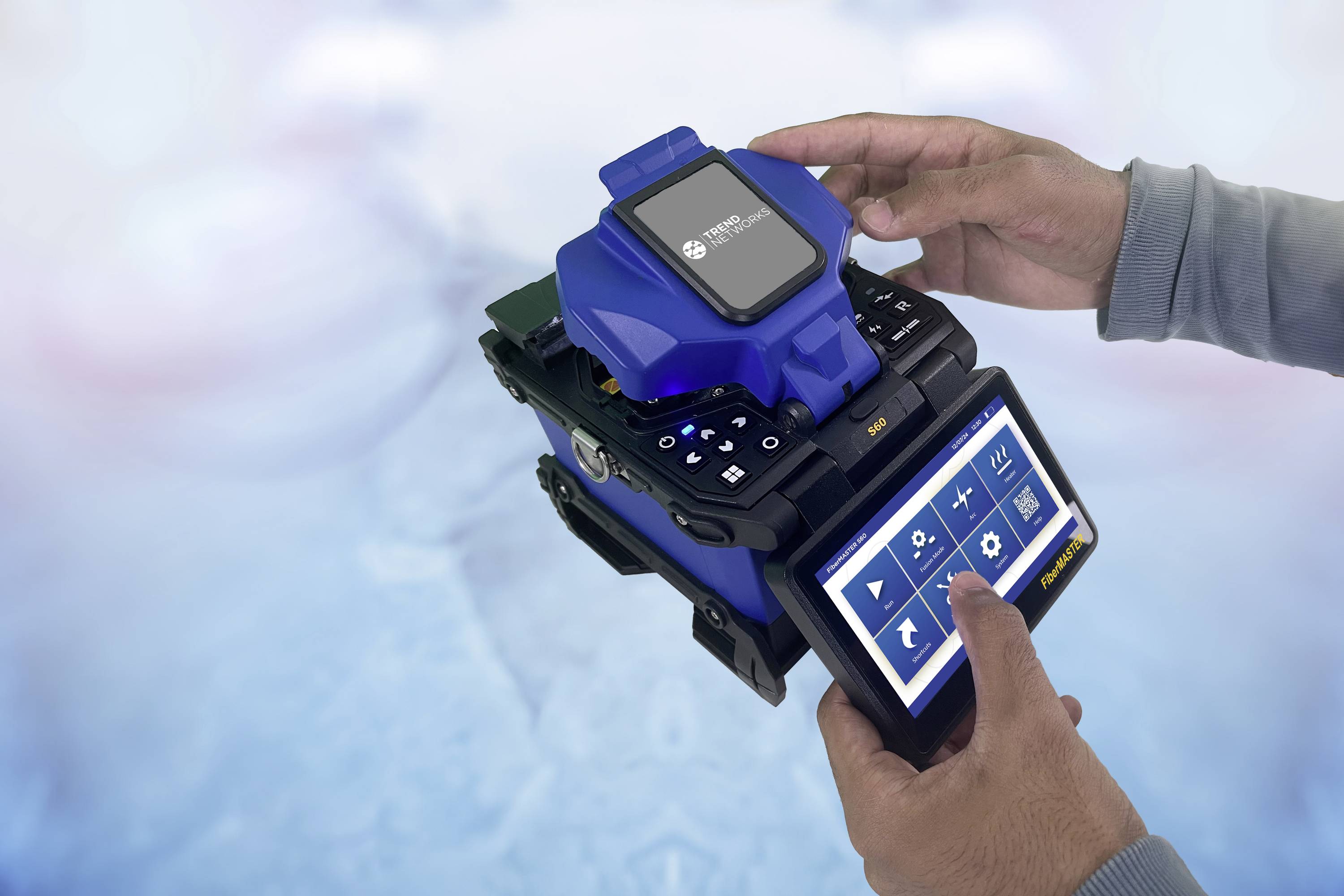 Two hands are operating a blue technical device with a display and multiple control elements, which appears to be used for fibre processing.