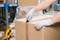 A person wearing grey gloves is opening a large cardboard box with a knife in a warehouse. Storage shelves are visible in the background.