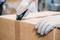 A person wearing gloves opens a cardboard box with a Stanley knife.