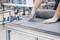A person wearing gloves is cutting grey fabric on a table in a factory environment. The focus is on precise manual work.
