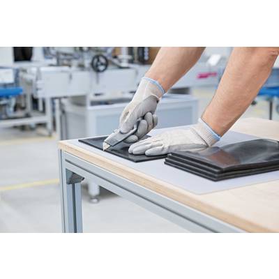 A person is cutting a piece of black material with a craft knife on a table in a factory environment.