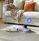 A vacuum cleaner robot navigates around slippers in front of a sofa. A light signal indicates its cleaning and obstacle avoidance capabilities.