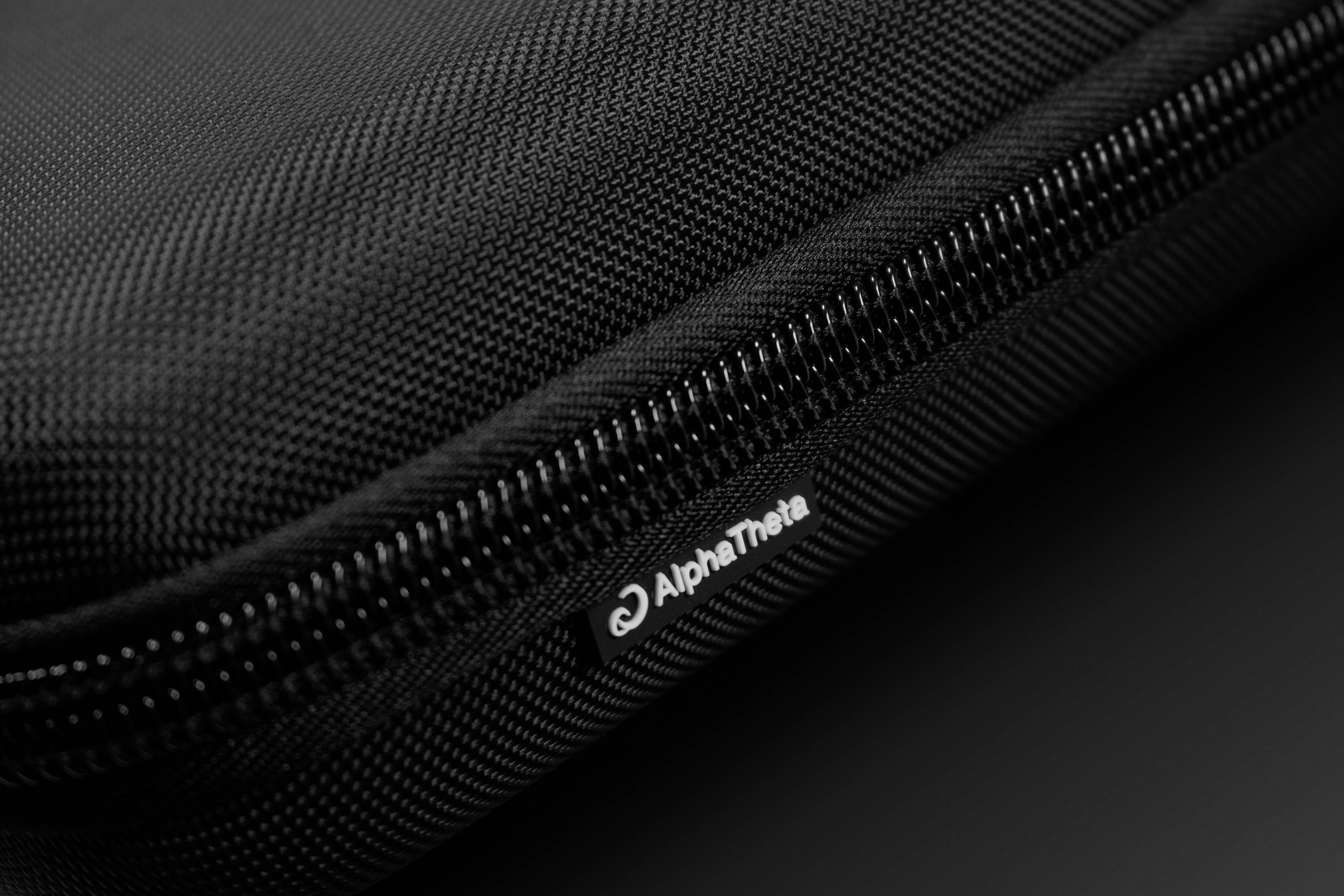 Close-up of a black zip on a bag. Beside it, a label reading 'AlphaTheta'.