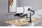 A desk with two monitor arms holding a laptop and monitor. In the background, a grey chair and an abstract artwork.