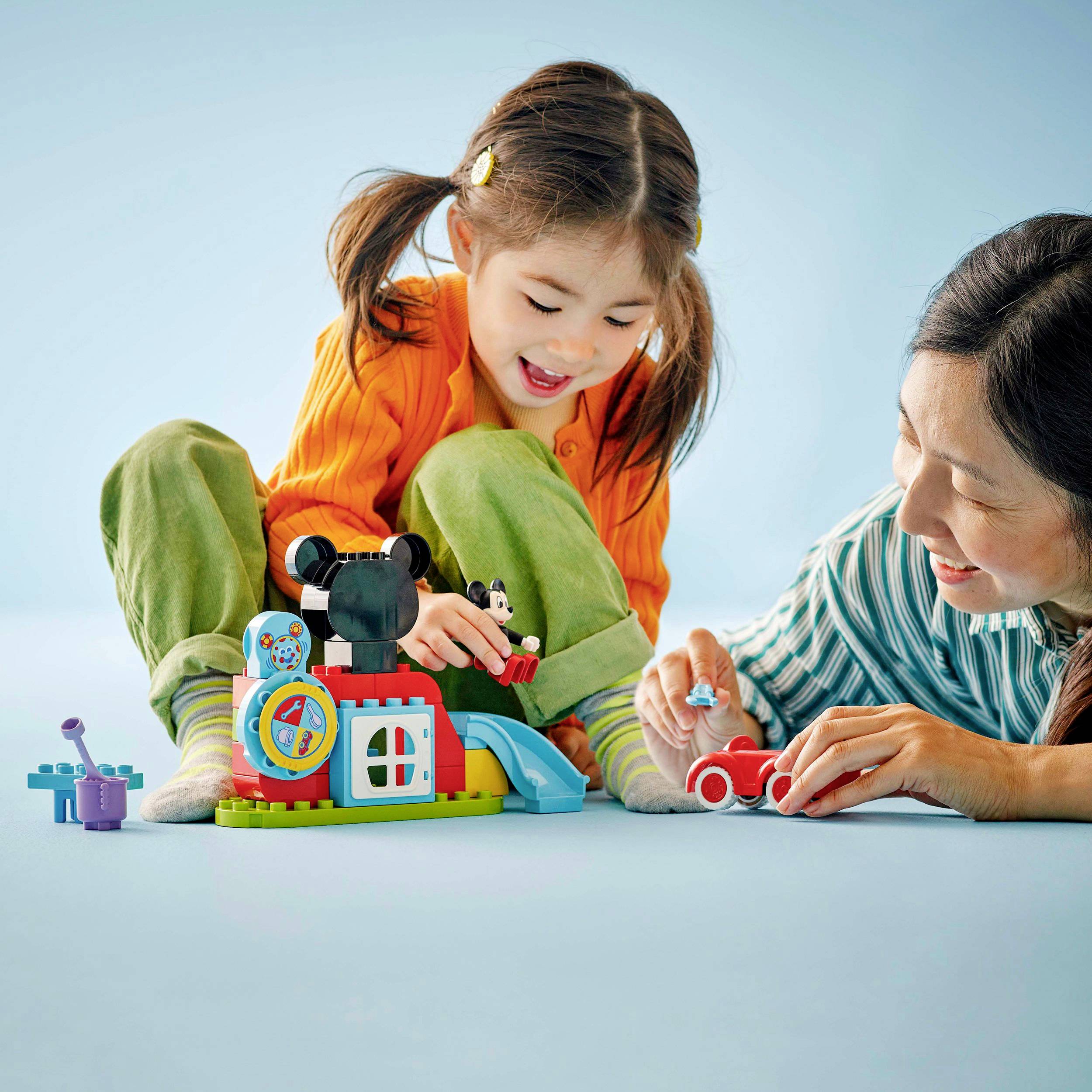 A smiling child plays with colourful building blocks, including a carousel figure and a car, supported by an adult.