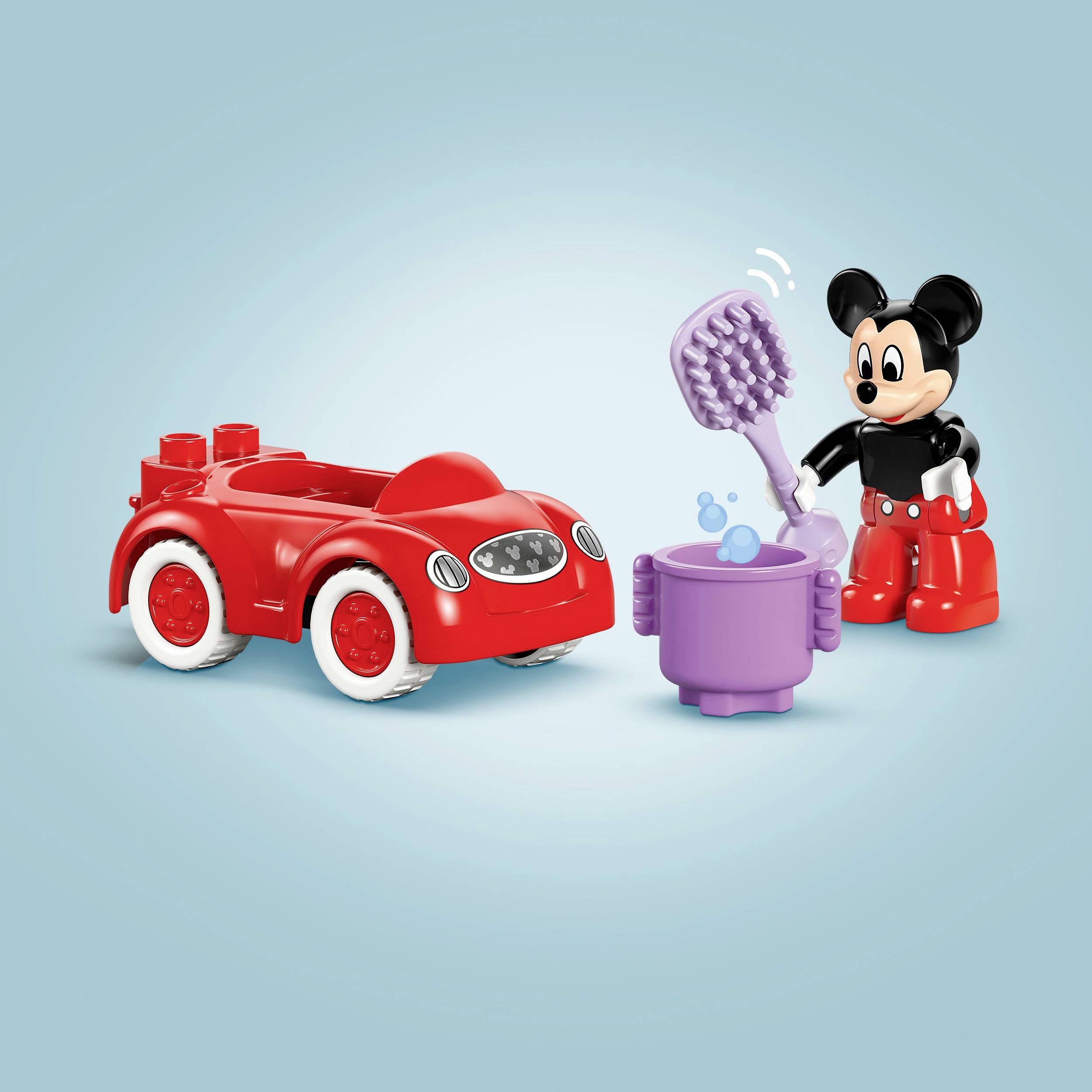 A red toy car and a figure with large ears are holding an oversized toothbrush. A purple cup stands beside them on a blue background.