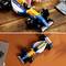 Two LEGO racing cars on a table, one being assembled. The cars are blue and yellow with 'eleven' stickers. A person is pointing at a detail.