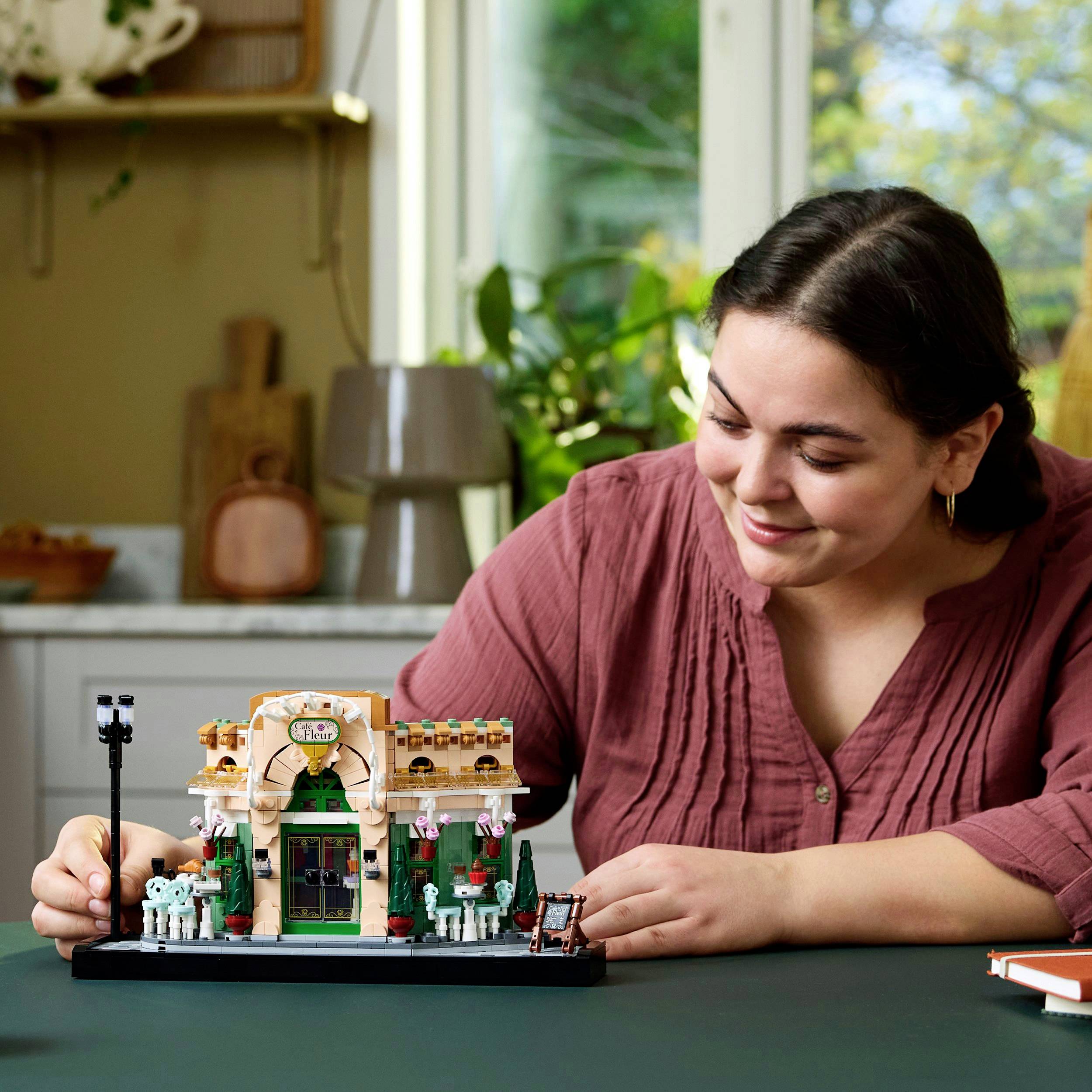 A person is smiling and sitting at a table with a detailed miniature model of a Mexican restaurant.