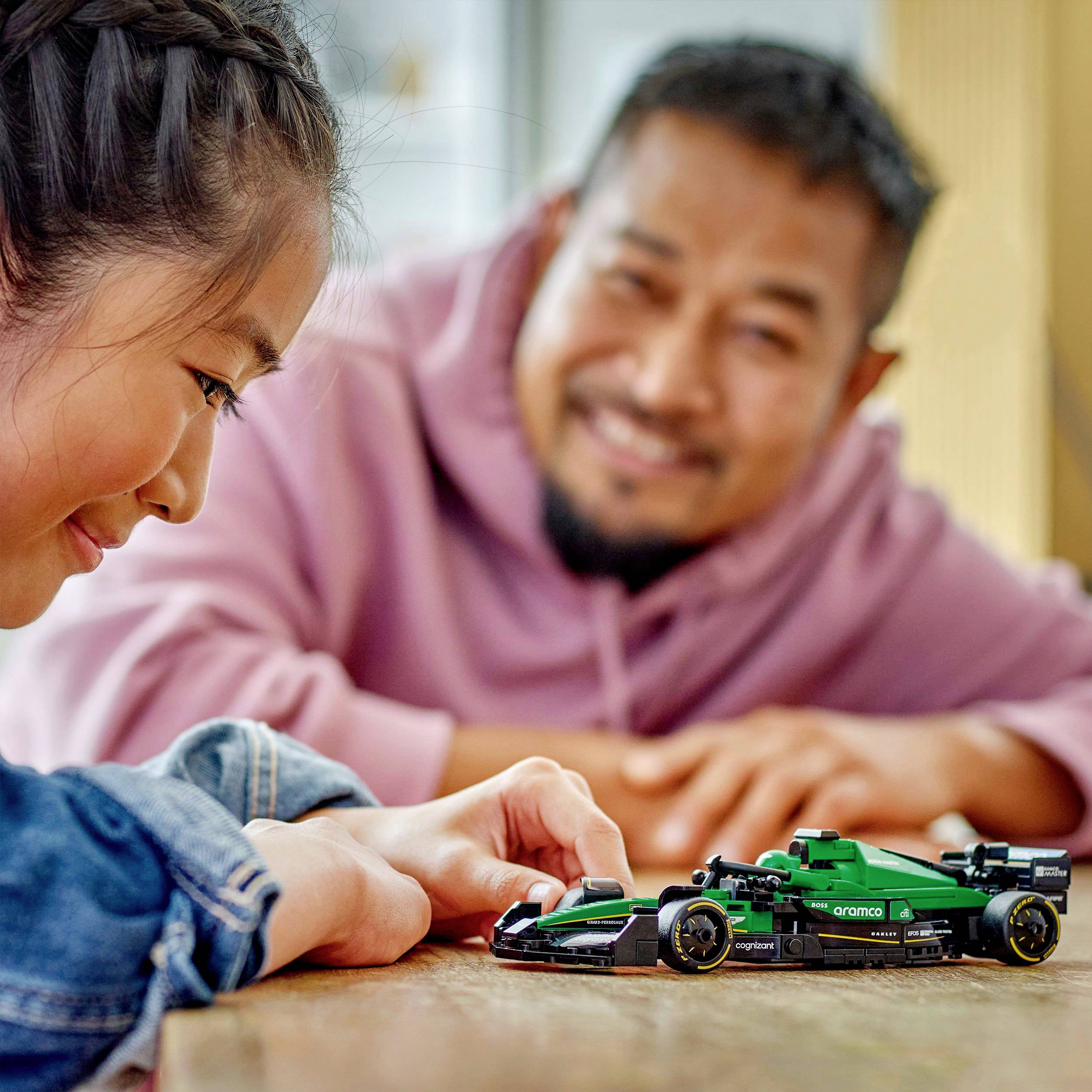 A smiling woman and a man are looking together at a small model car on a table, which they are observing with enthusiasm.
