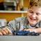A child is smiling whilst playing with a blue toy racing car on a table. The child appears focused and seems to be thoroughly enjoying themselves.