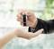 A hand passes a key onto an outstretched palm. Background blurry and greenish. Symbolises transfer.