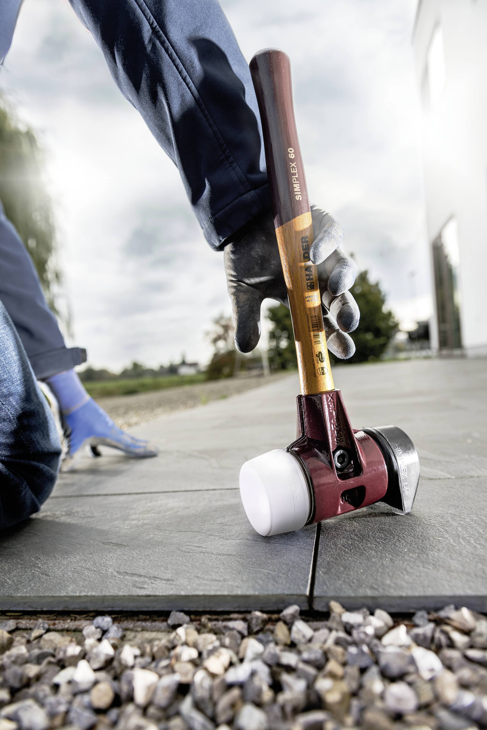 A person is laying outdoor tiles with a hammer while wearing protective clothing and gloves.