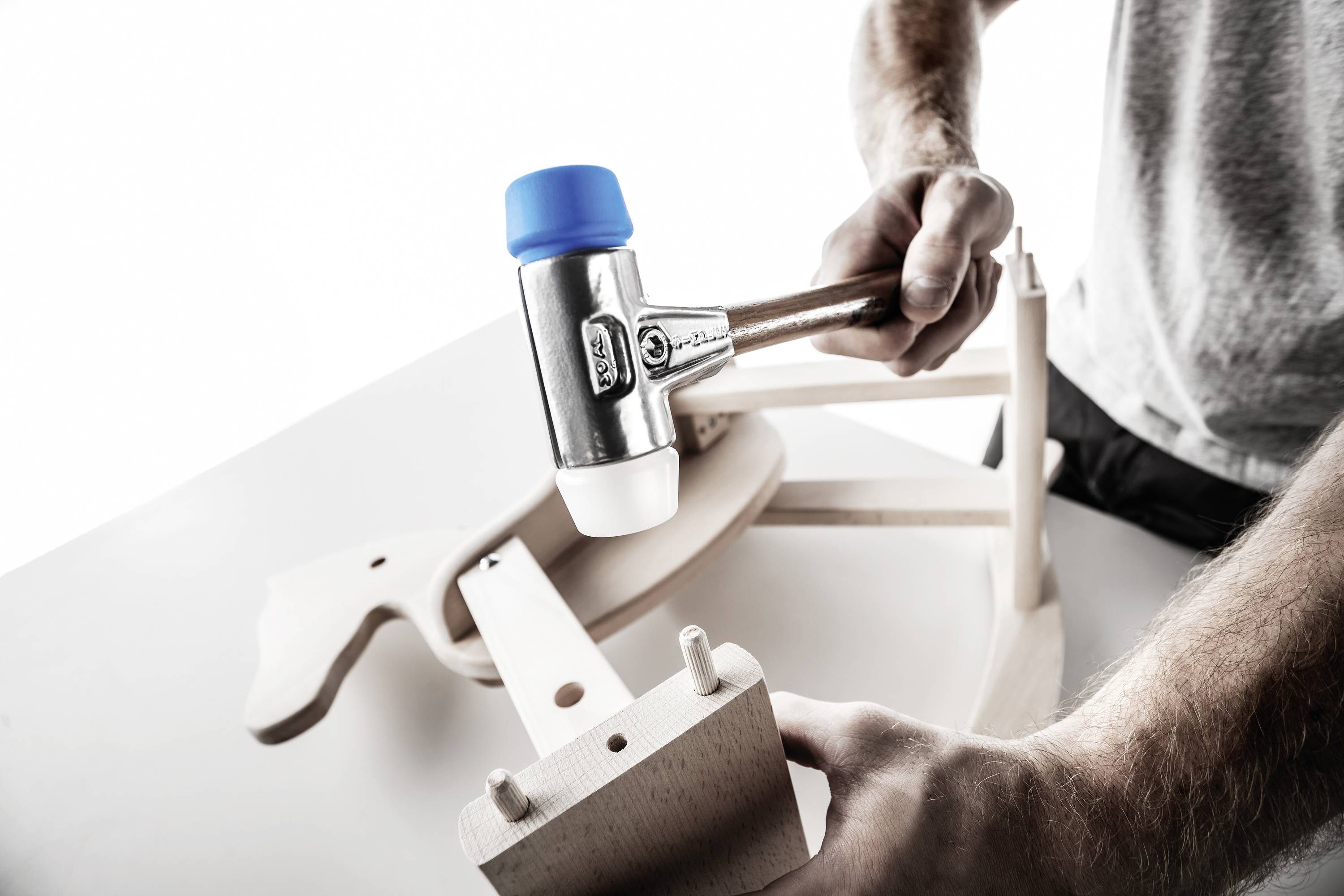 A person is assembling a wooden toy with a rubber mallet. The focus is on installing precise wooden joints.