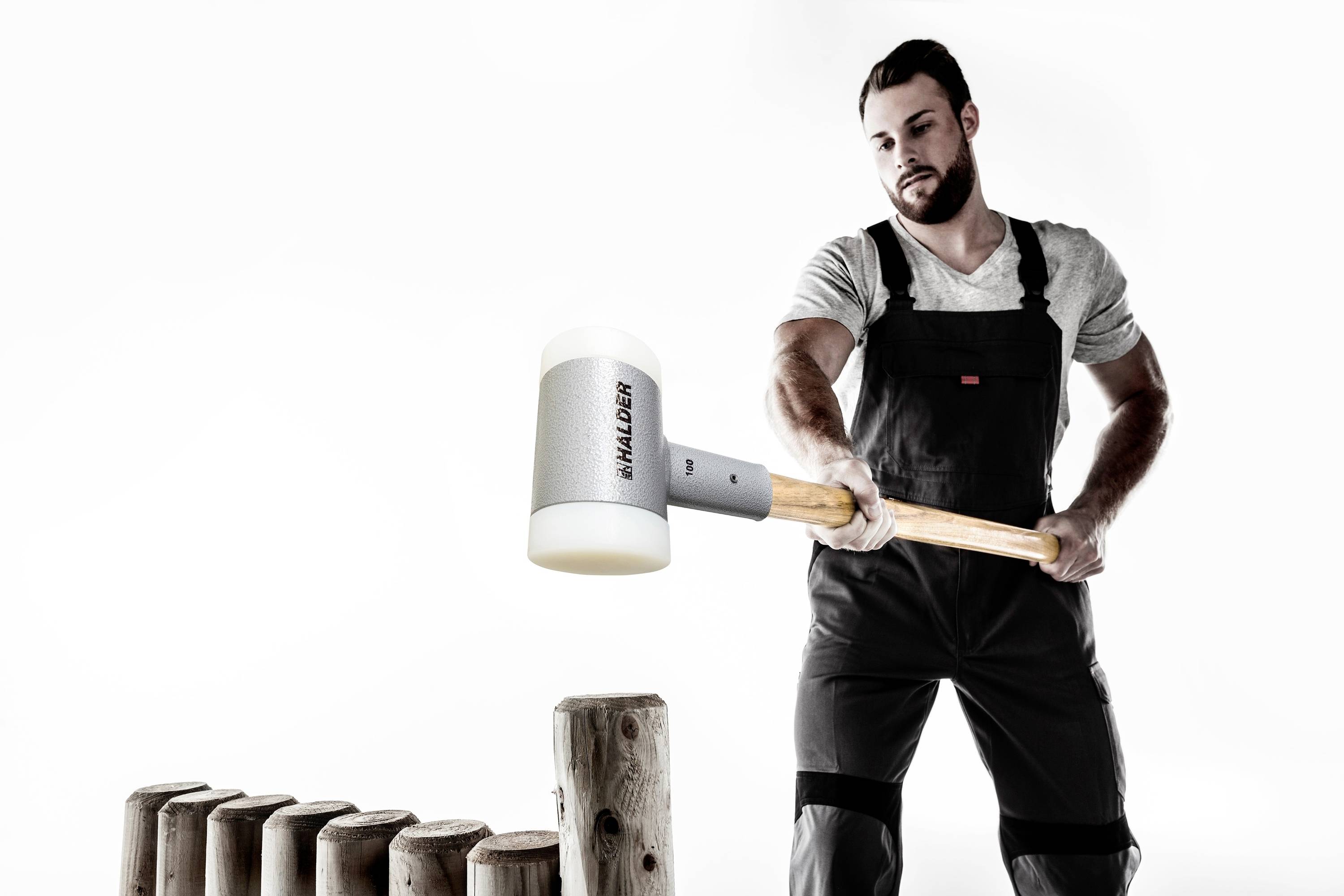 A man in workwear is using a large hammer to work on wooden stakes. The scene depicts skilled manual labour.