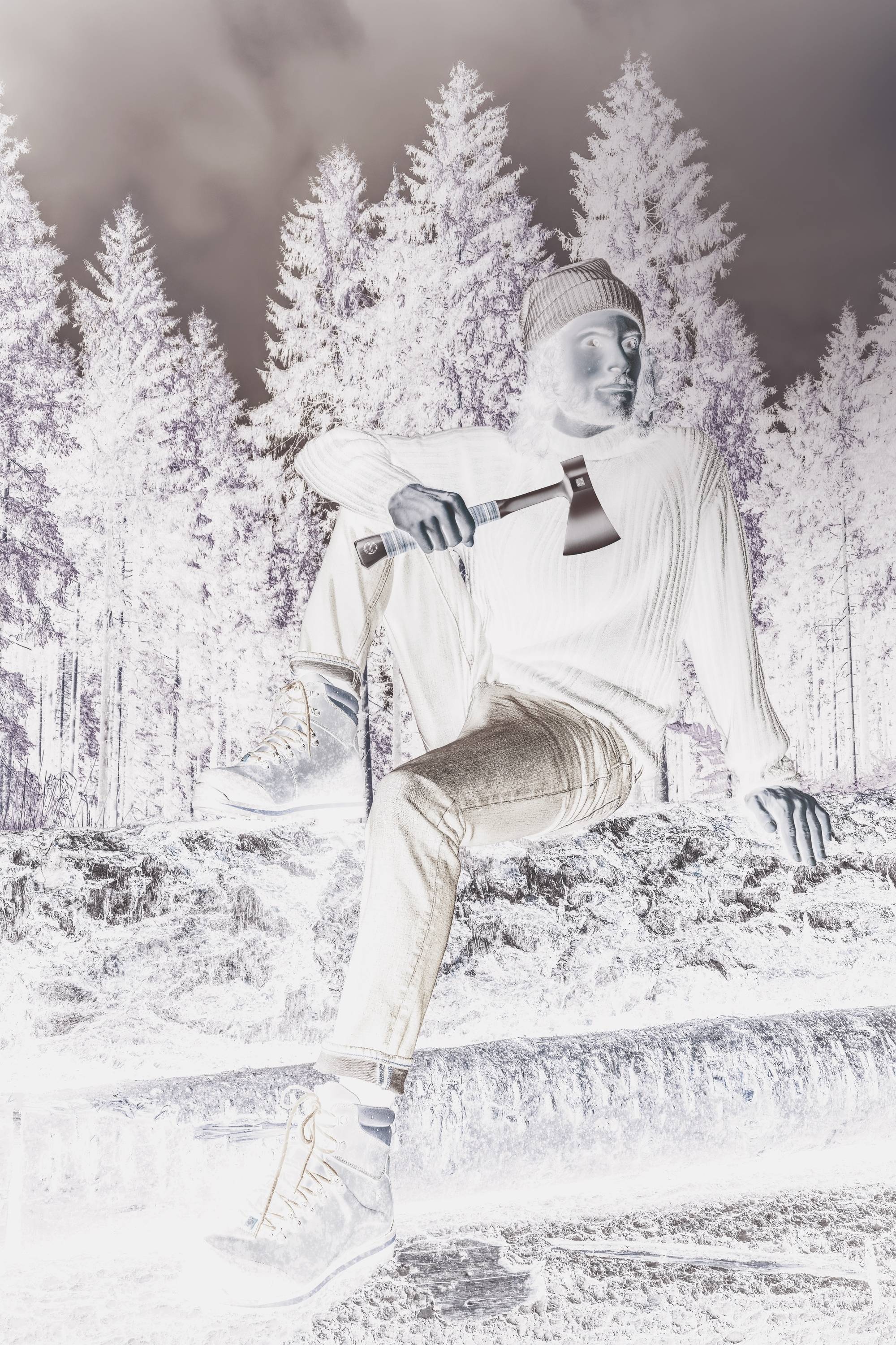 A person in casual clothing sits outside on a tree trunk, holding an axe, with a wooded backdrop.