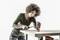 A person with curly hair is working carefully with a hammer on a copper pipe placed on a wooden table.