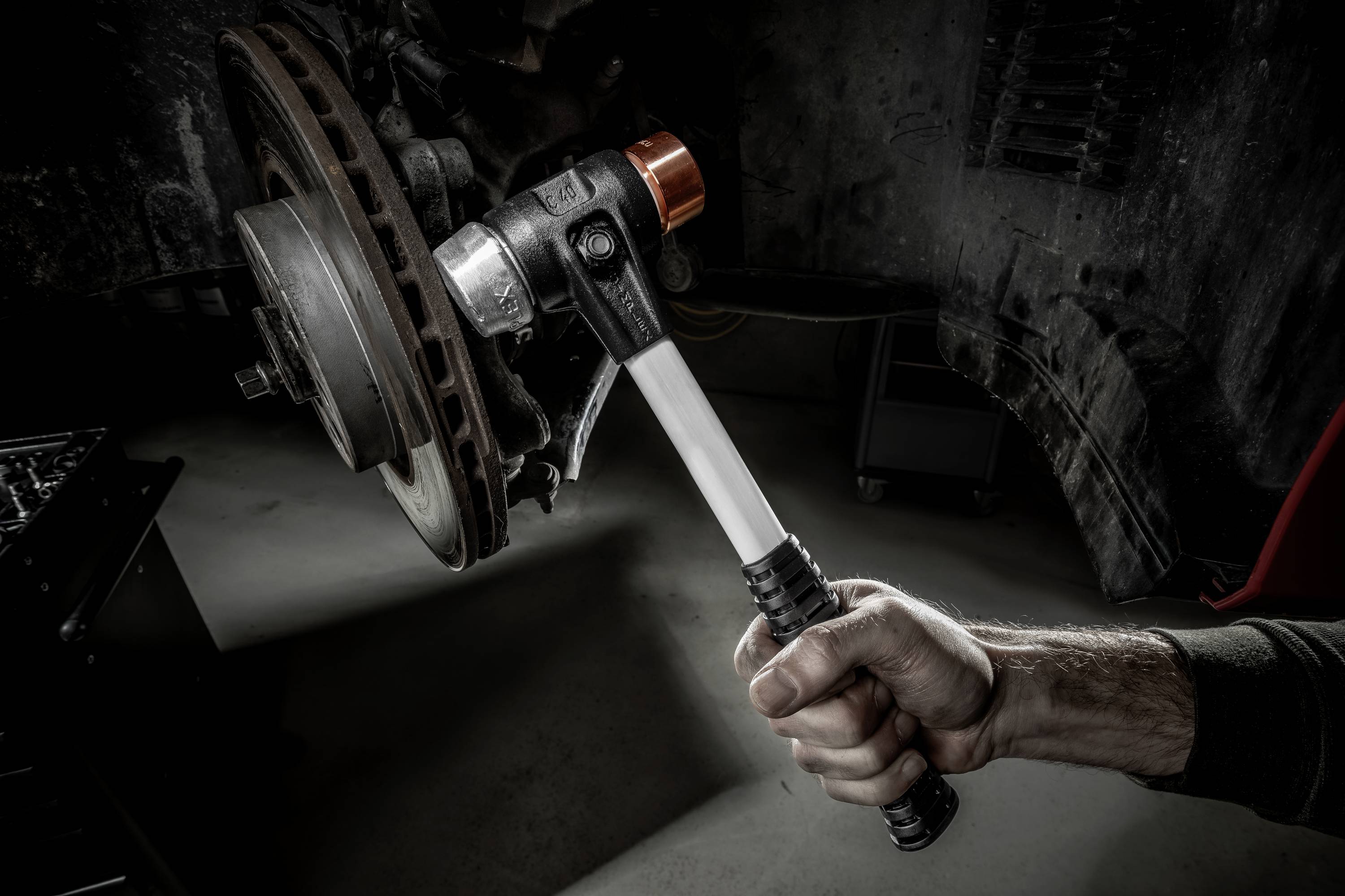 A mechanic's hand is holding a torque wrench next to a car wheel, ready for adjustment. The image depicts a workshop context.