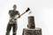 A man in a T-shirt and trousers raises an axe to split a wooden block on a tree stump.