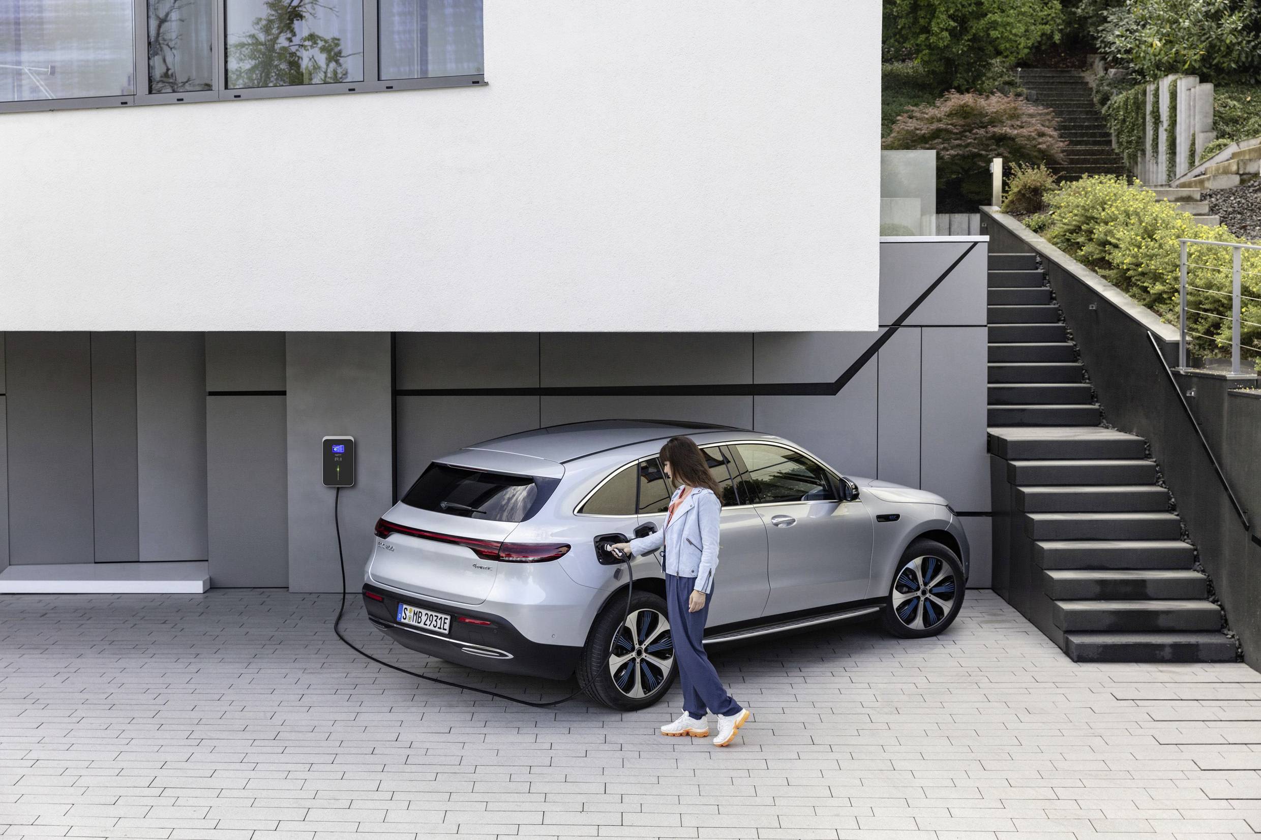 A person is charging an electric car at a charging station next to a modern building.