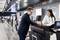 A man and a woman are standing at an airport check-in desk. The man hands documents to the woman while she assists him.