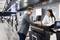A man is speaking to a woman at a counter in a modern airport or office. The environment appears bustling and technological.