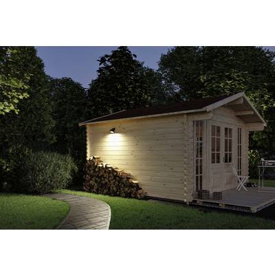Wooden garden shed at night, with a stack of firewood beside it and a paved pathway running in the foreground. Exterior lighting on the shed.