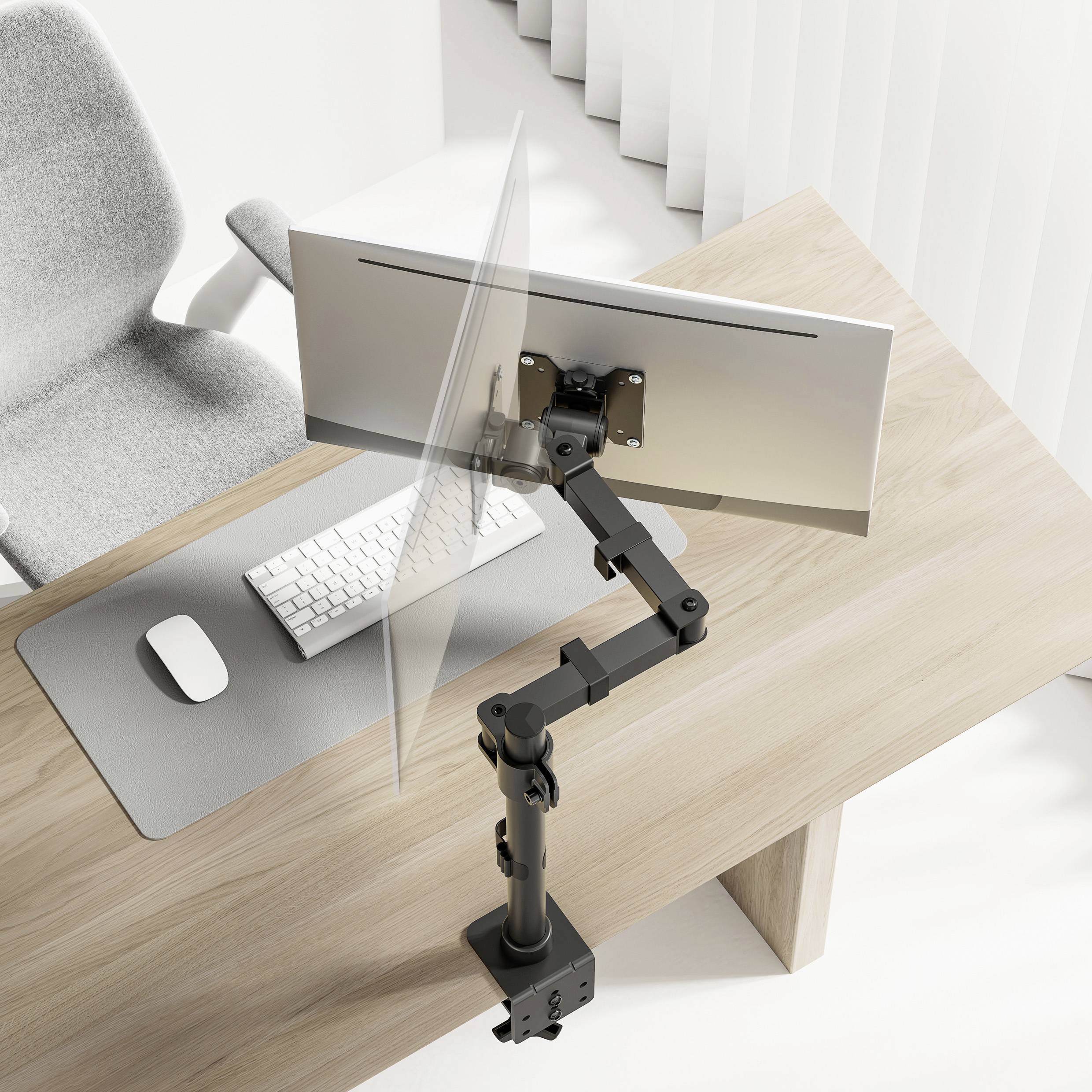 A desk with an ergonomic monitor mount holding a screen above a keyboard and mouse. A grey office chair stands beside it.