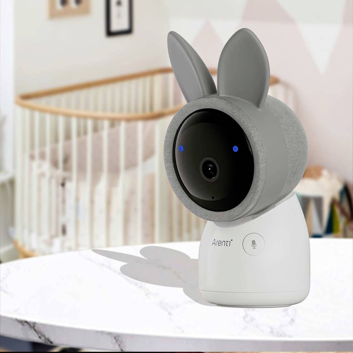 A bunny-shaped baby camera sits on a table. In the background, a cot can be seen, indicating a child's bedroom.