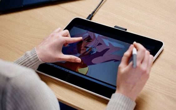 A person is drawing on a tablet using a stylus and finger. On the screen, a face with pink hair is visible.