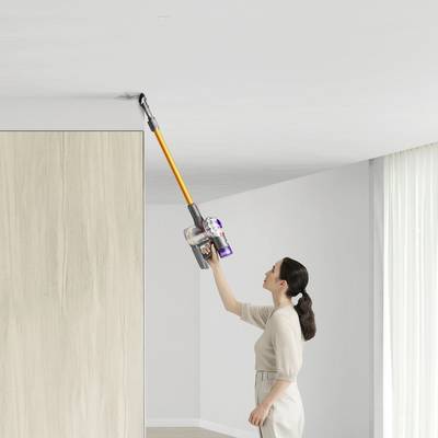 A woman is cleaning the ceiling with a cordless vacuum cleaner in a bright, modern room.
