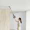 A woman is cleaning the ceiling with a cordless vacuum cleaner in a bright, modern room.