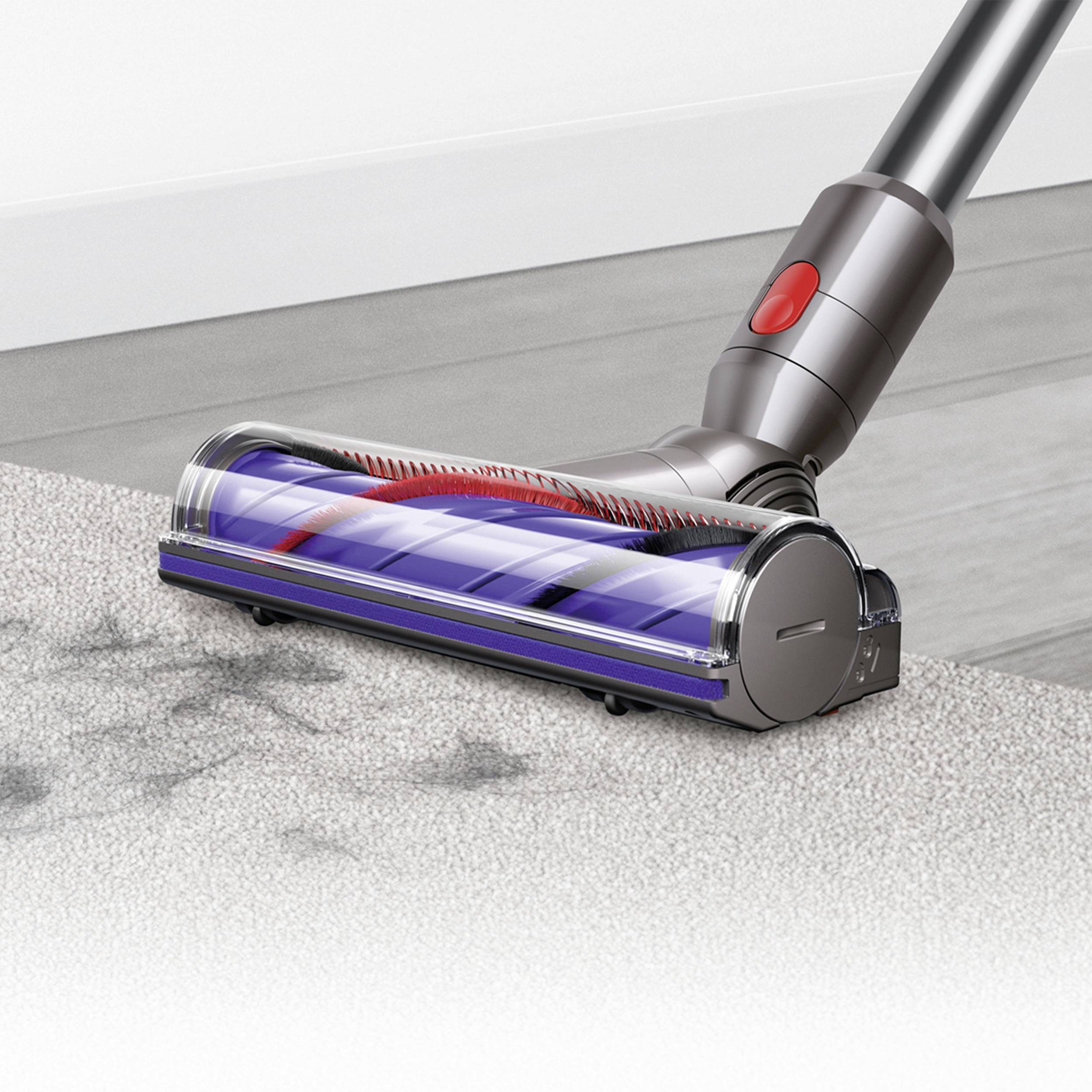 A vacuum cleaner is sucking dirt from a carpet. The vacuum's brush head is visible and in operation.