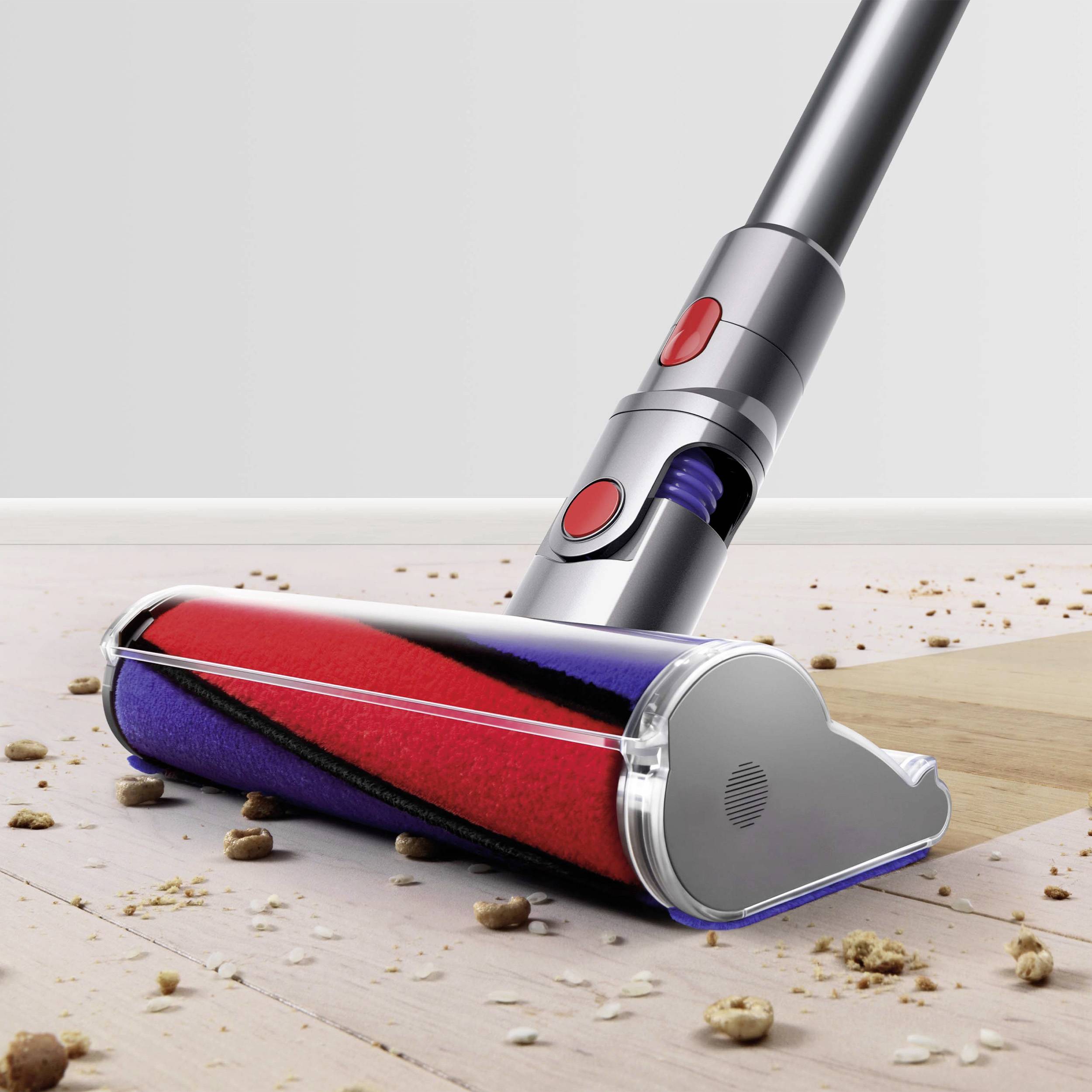 A vacuum cleaner with a red and blue brush roller is vacuuming crumbs from a hard floor.