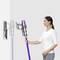 A person is using a cordless vacuum cleaner, which is taken from a wall mount. The vacuum cleaner has a purple tube.
