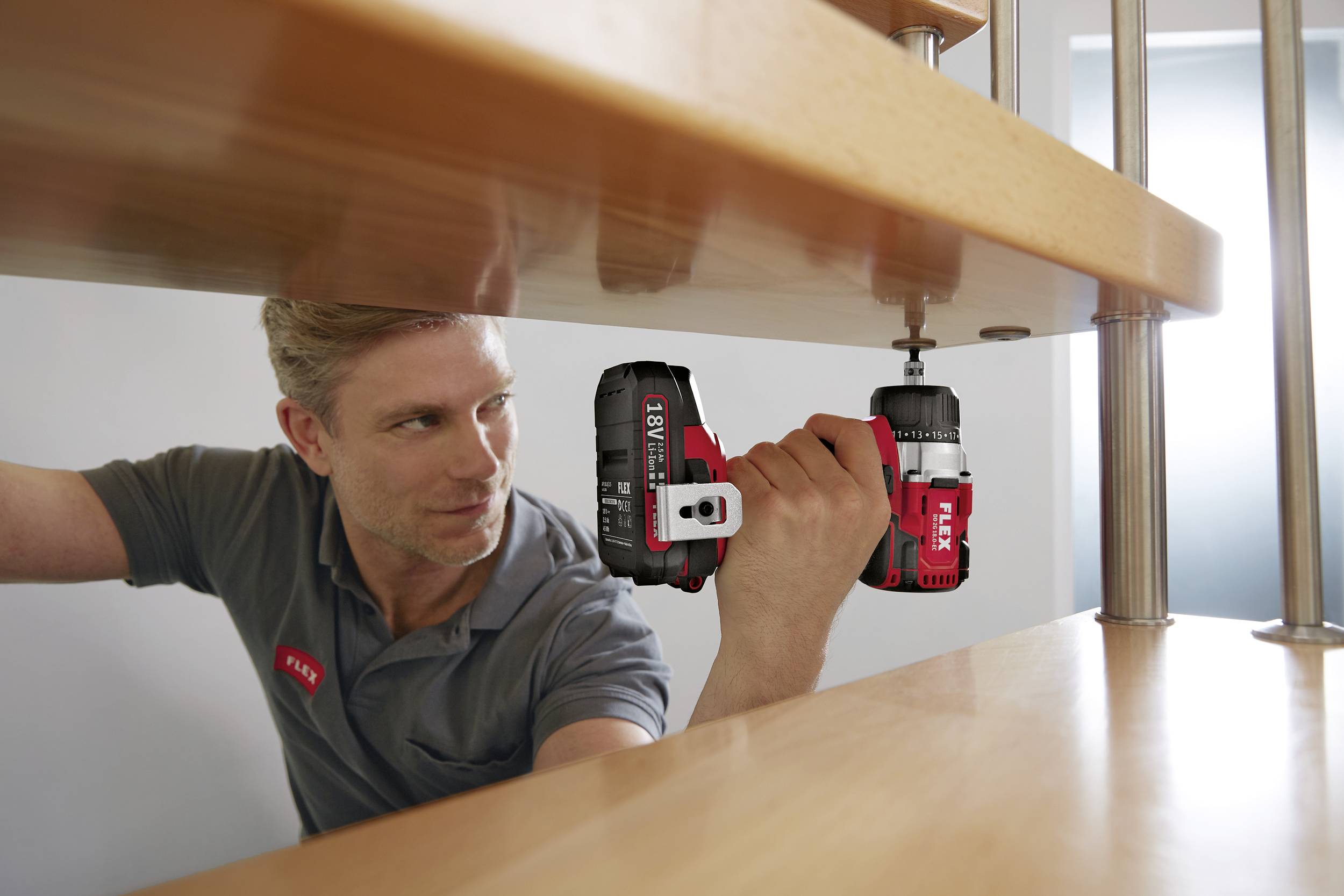 A man is installing a staircase with a cordless drill, wearing a grey shirt with a name badge.