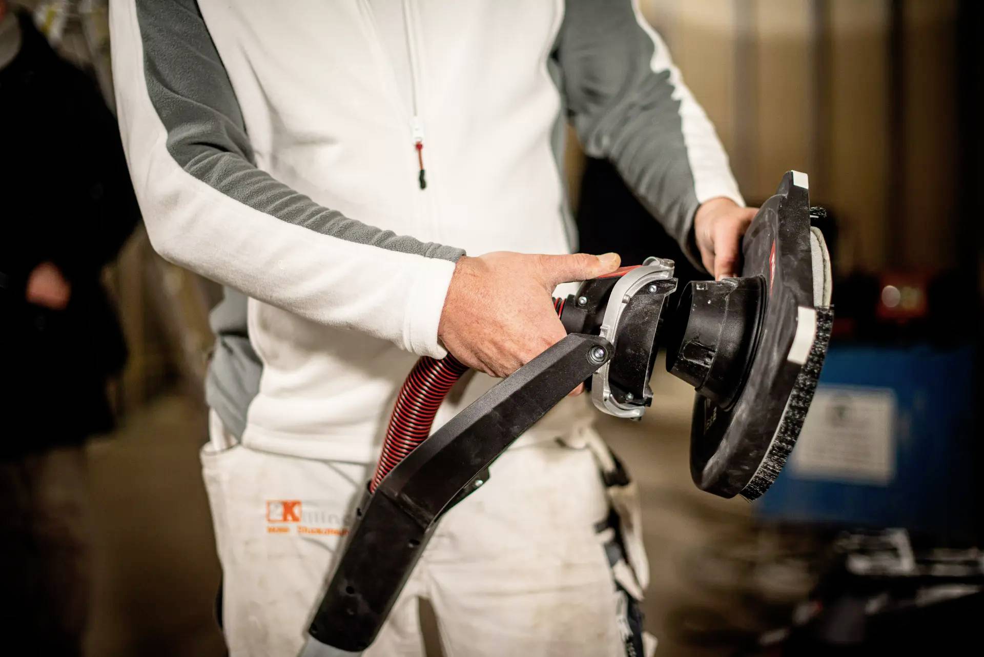 A person is holding an angle grinder with both hands. The working environment suggests a construction or renovation scenario.