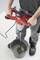 A person is mixing cement or a similar mixture in a bucket using an electric mixer. The mixer has a red handle.