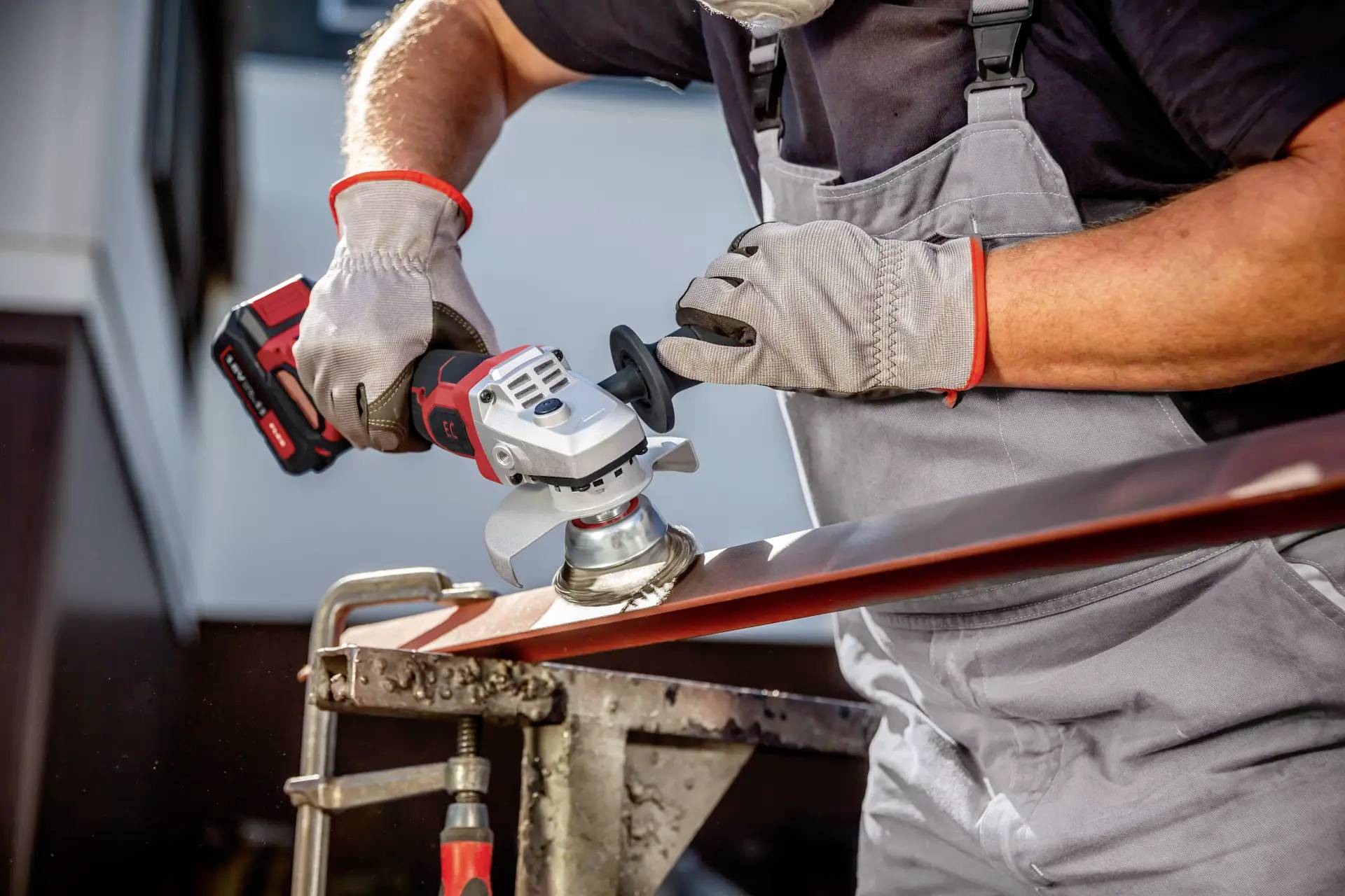 A craftsman in protective gear is grinding a metal piece with an angle grinder.