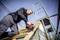 A worker on a construction site is using an electric tool to secure wooden battens. Scaffolding can be seen in the background.