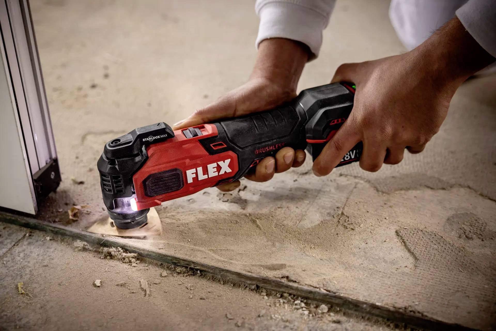 A person is using an oscillating multi-tool to cut a gap in the floor along the door threshold.