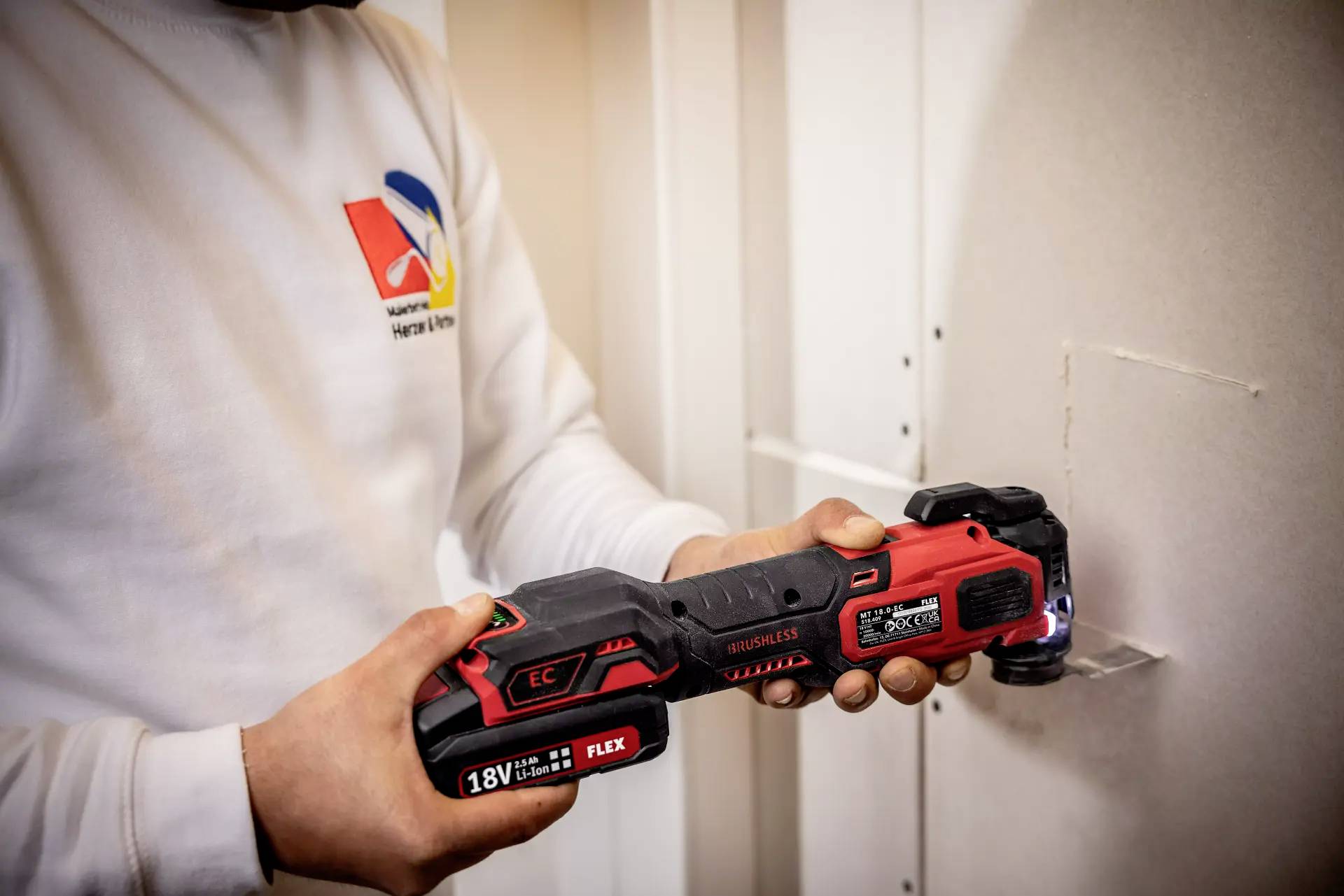 A person is using an electric multi-tool to cut a hole in a white wall.