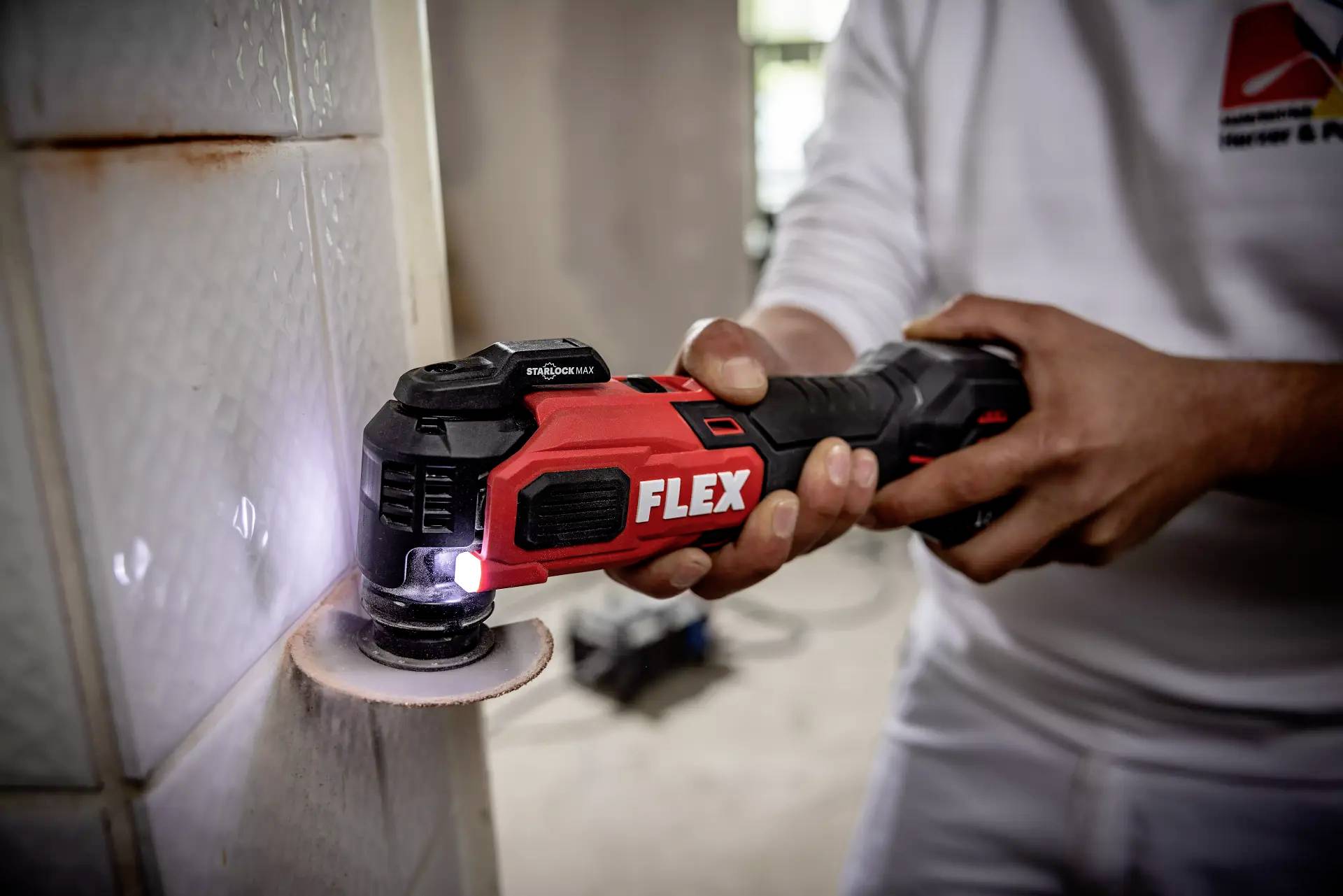 A person is using an electric tool branded 'FLEX' to cut grooves in white-tiled walls.