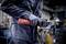A person in work attire is holding an electric tool in their hand, presumably an angle grinder, in a workshop environment.