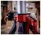 Close-up of a red tripod with a black smartphone attached to the side. Scene depicts a workshop environment.