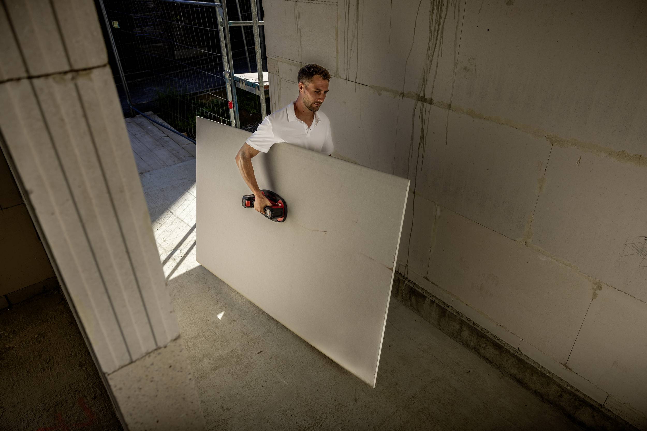 A person is cutting a large white board with an electric tool in a semi-finished room with a concrete floor.