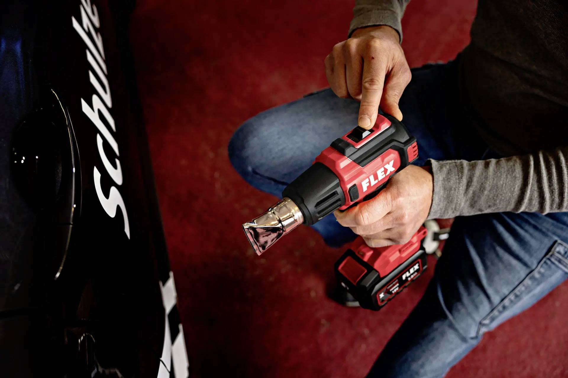 A person is using a red tool to polish a black car. The 'Schulte' lettering is visible on the side of the car.