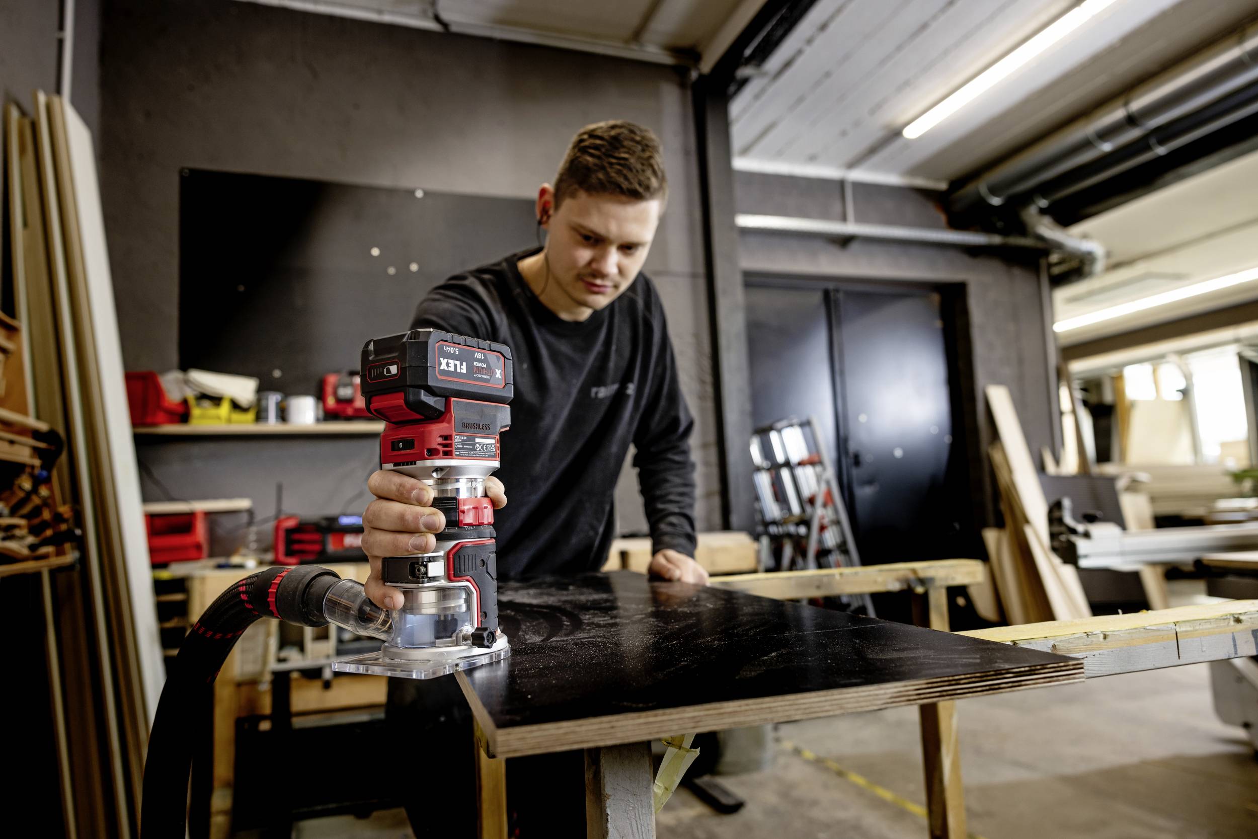 A man is sanding a dark wooden board with an electric sander in a workshop. Tools are visible in the background.